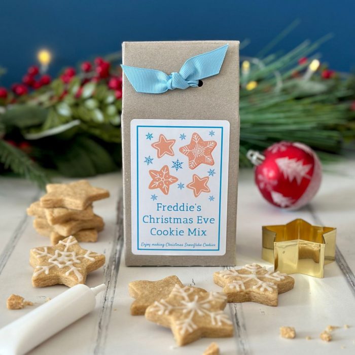 Snowflake biscuit mix box in blue with cutter, icing and baked biscuits in the foreground