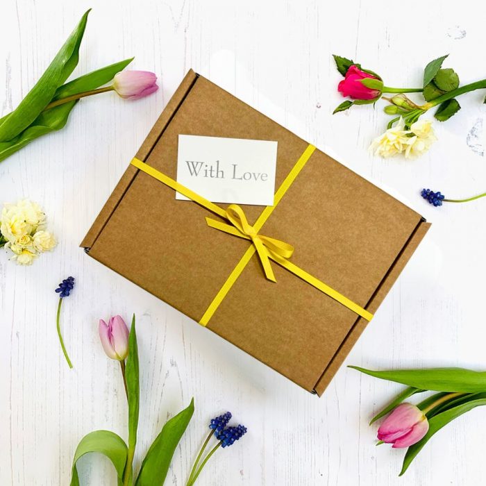 Gift box tied with yellow ribbon, gift tag and flowers decorating the background