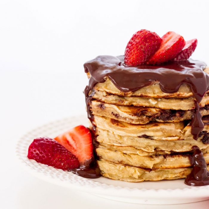 Chocolate chip pancake stack with chocolate sauce and strawberries.